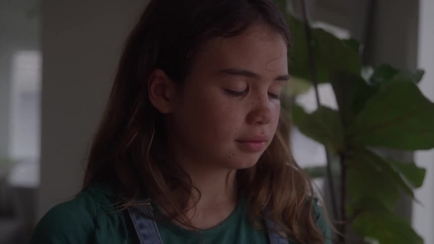 Girl touches her face with an introspective expression near a bright window