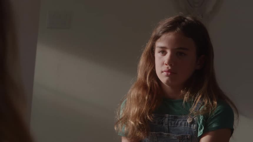 Girl in denim overalls looks at her reflection in the mirror under soft light