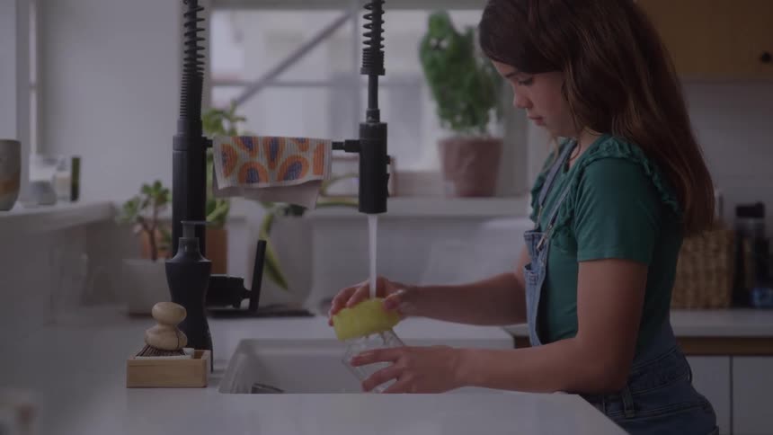The girl is cleaning a glass in the sink