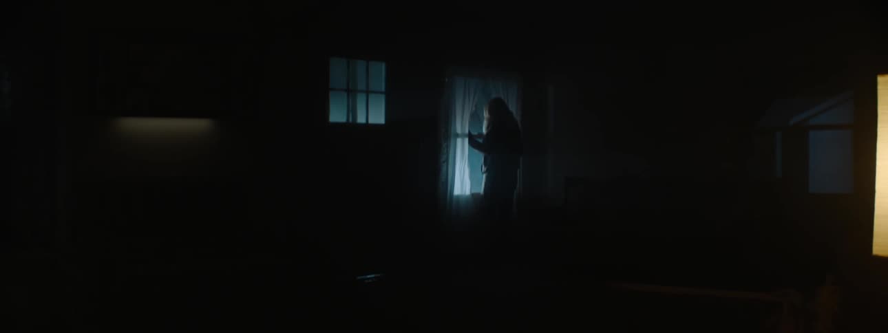 A woman gets off the couch and looks out the window