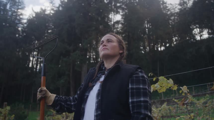 Woman holds a rake and looks up at the sky amidst a field