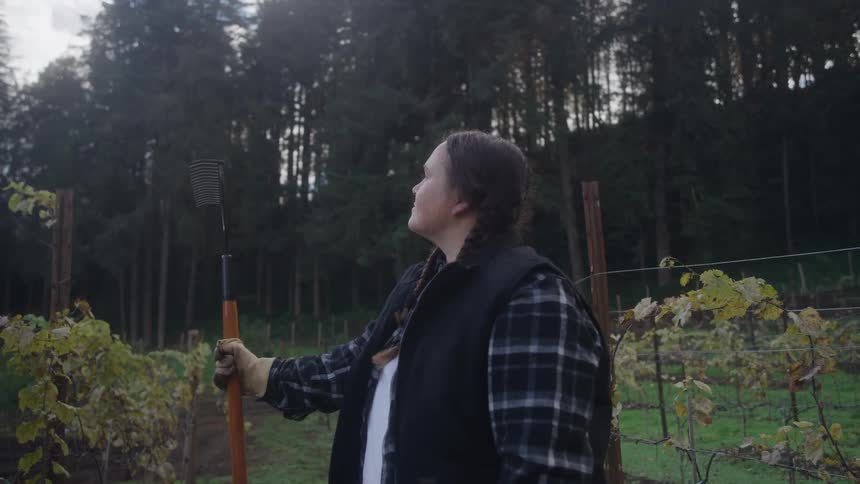 Female gardener wearing a tartan shirt standing next to a garden holding a garden fork on her hand outdoors during day time