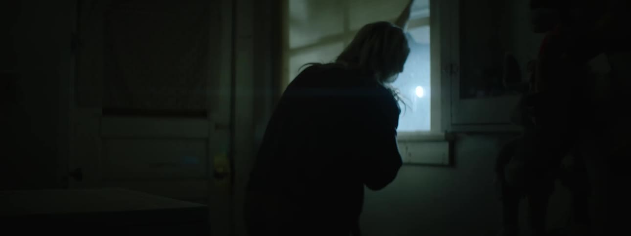 An older woman with long hair looks out of a window toward flashing lights