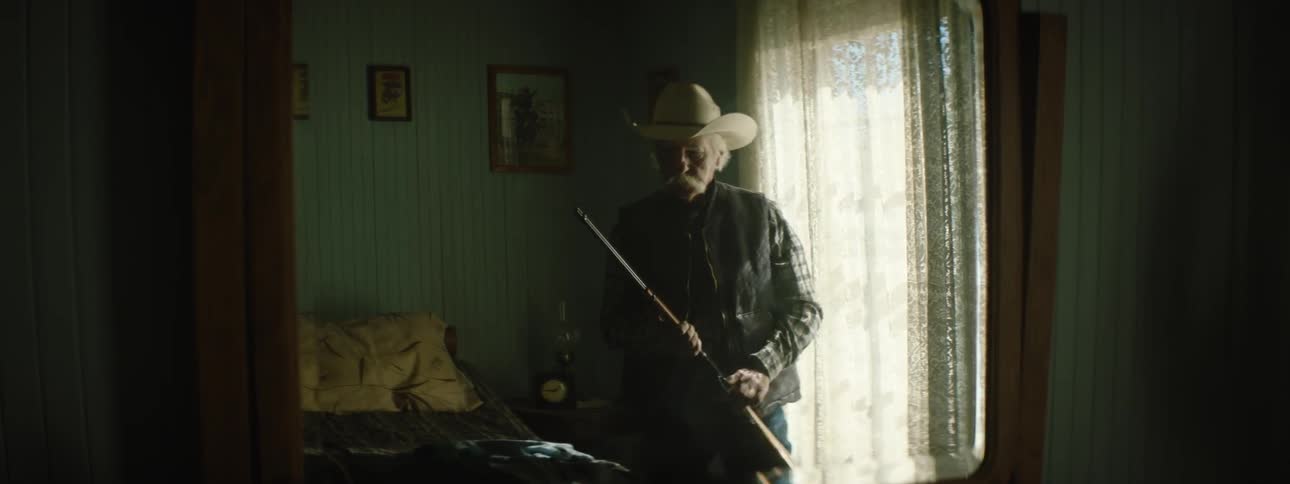 A man is holding a rifle in front of a window inside a house