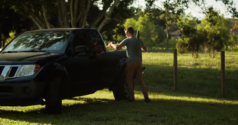 Man interacts beside black pickup truck parked on grassy area with trees in the background