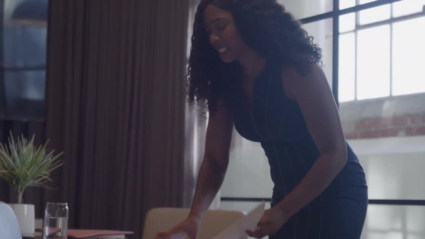 Woman standing at her desk in her office throws papers onto the floor after reviewing one document