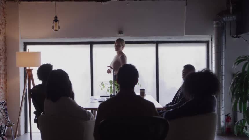 Person gives a presentation to a seated group in a room lit by large windows