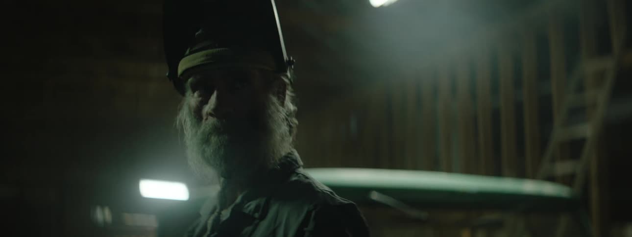 A man wearing a welding helmet looks out of his workshop