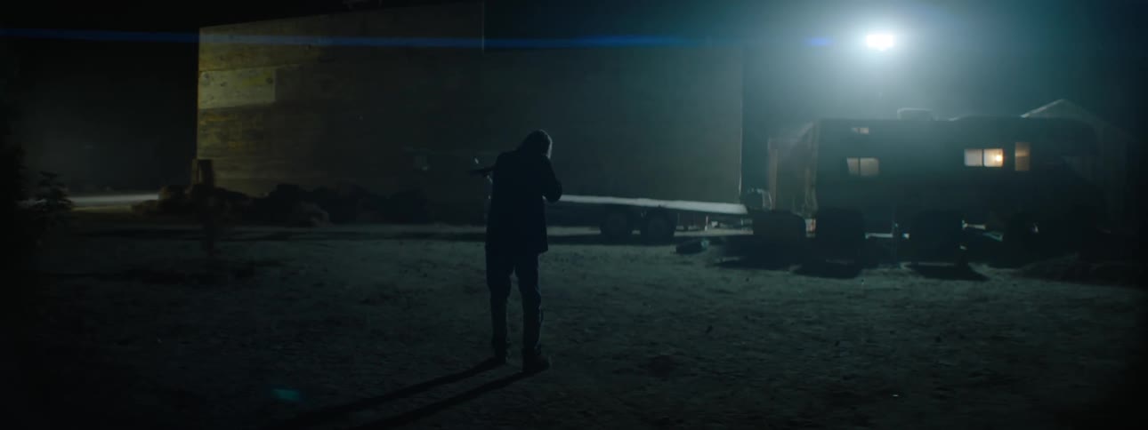 A man holds up a gun and walks outside at night