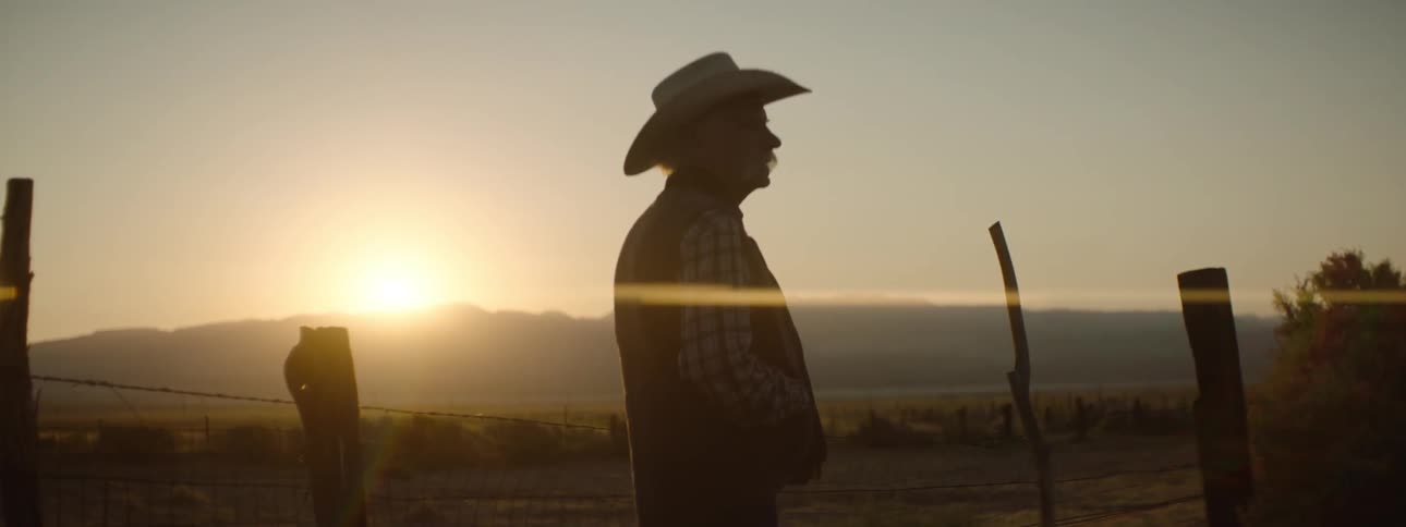 A man walks past a fence at sunset