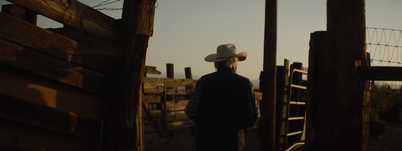 A man walks past a fence at sunset