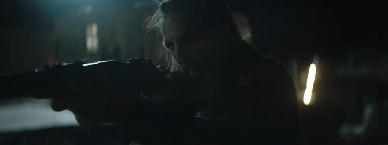 A man aiming a rifle searches outside at night
