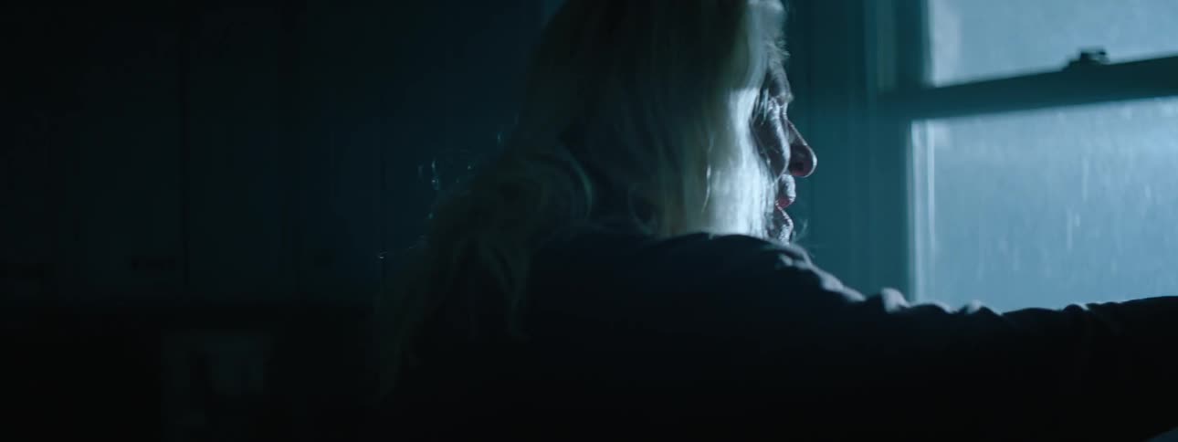 An elder woman looking around in a dark space with lights flashing outside