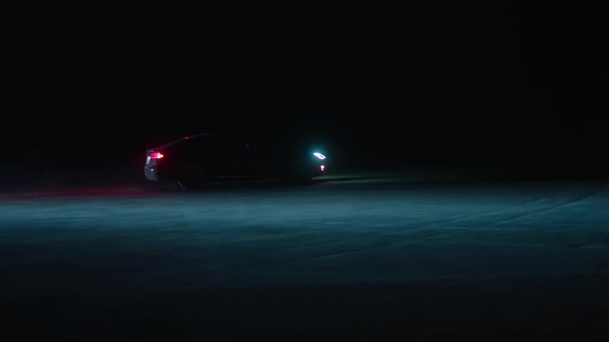 A car drives with its headlights on at night