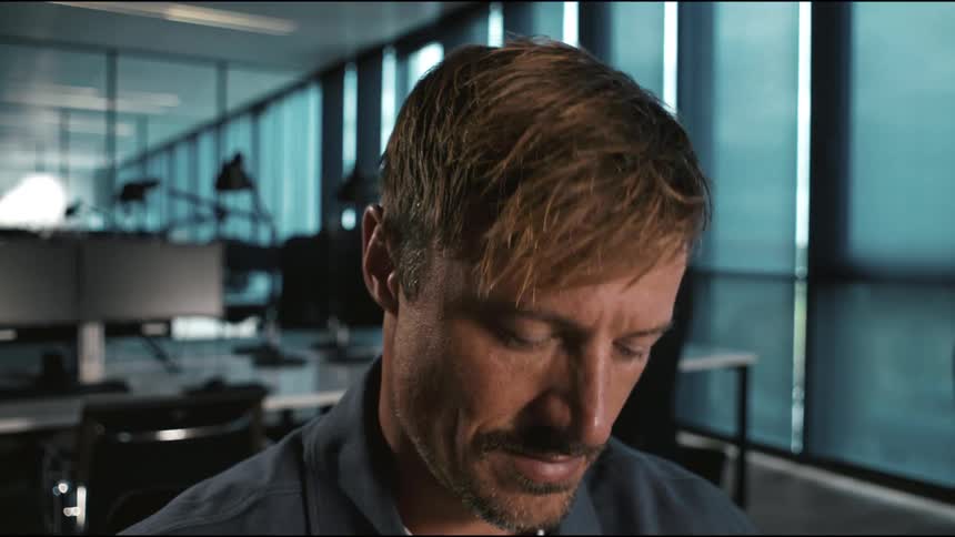 In a modern office a mans pensive expression softens into a subtle knowing smile