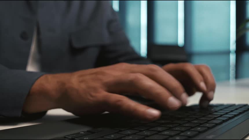 Male hands typing on a black keyboard in a corporate setting