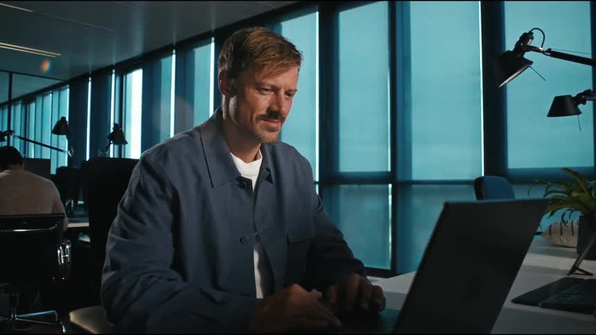Man focused reading on a laptop screen in a modern office