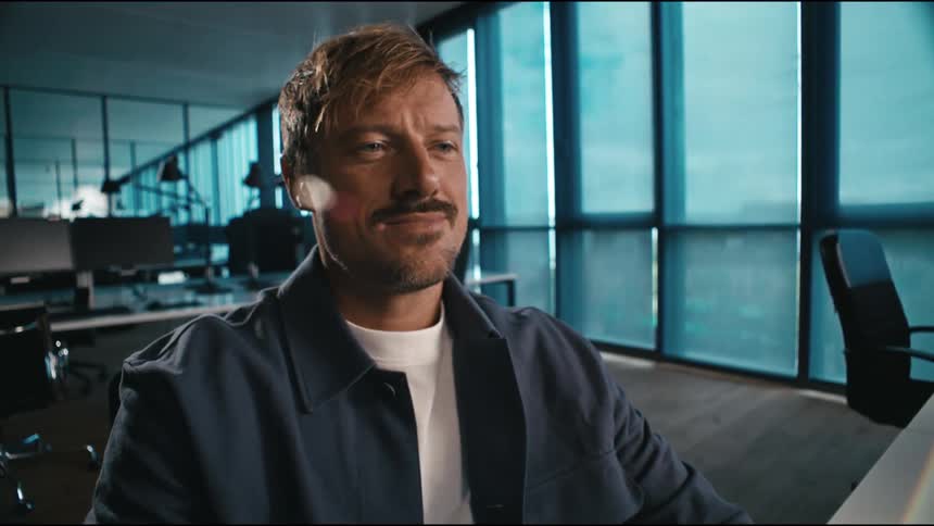 Man working on a desktop computer in an office building smiles