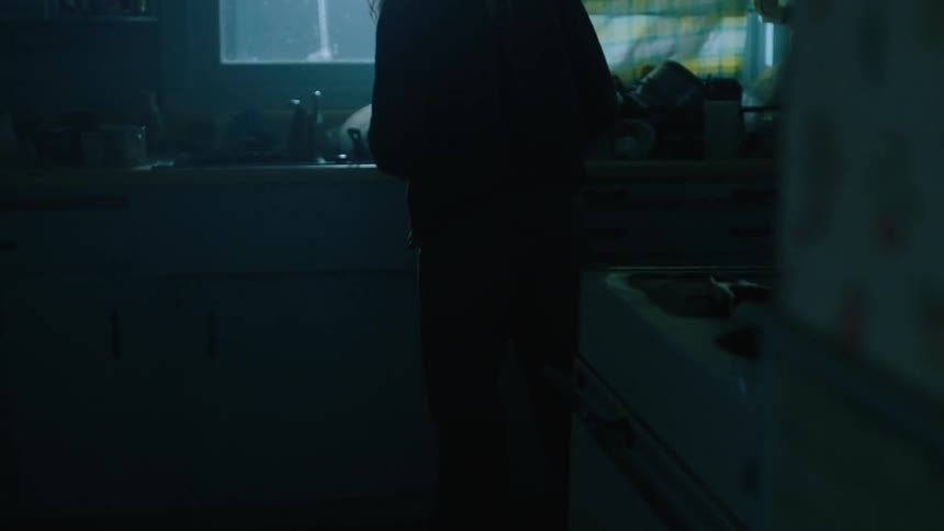 A woman walks in a dim kitchen