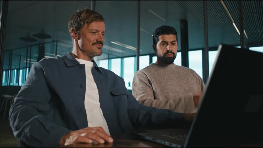 The man opens the laptop as a coworker thinks