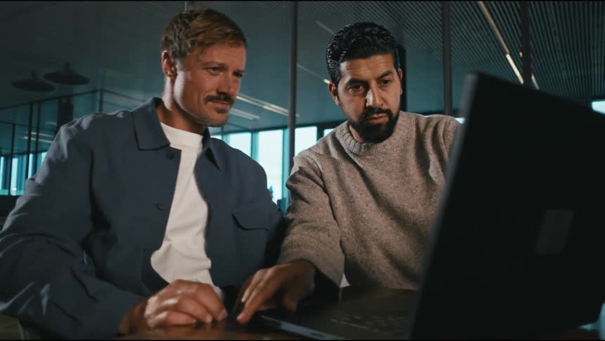 A man carries his laptop across the conference table to his colleague