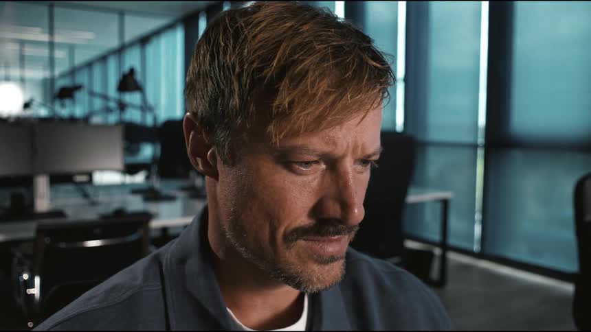 In a modern office a mans expression shifts from intense focus to a satisfied relieved smile