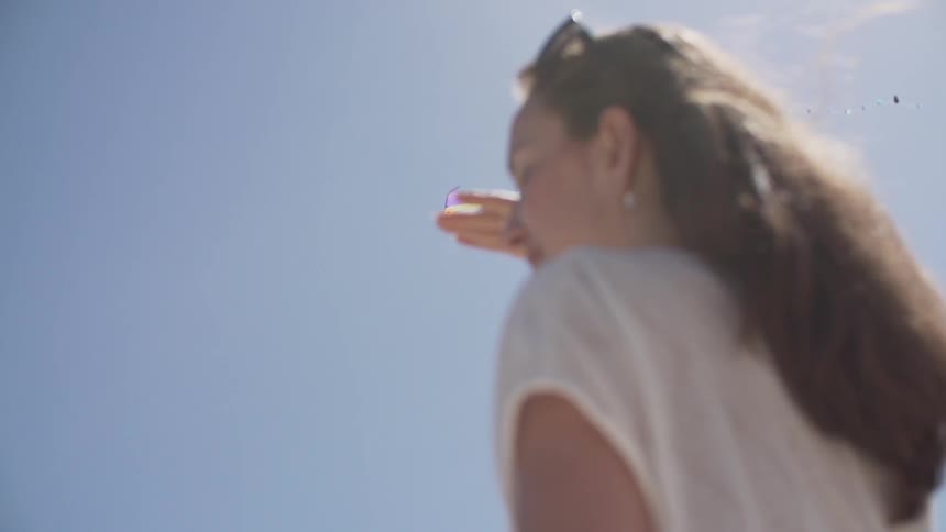 A woman looks up at a kite on a sunny day