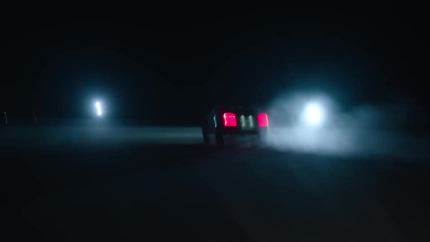 Car driving on pavement at night towards two bright lights