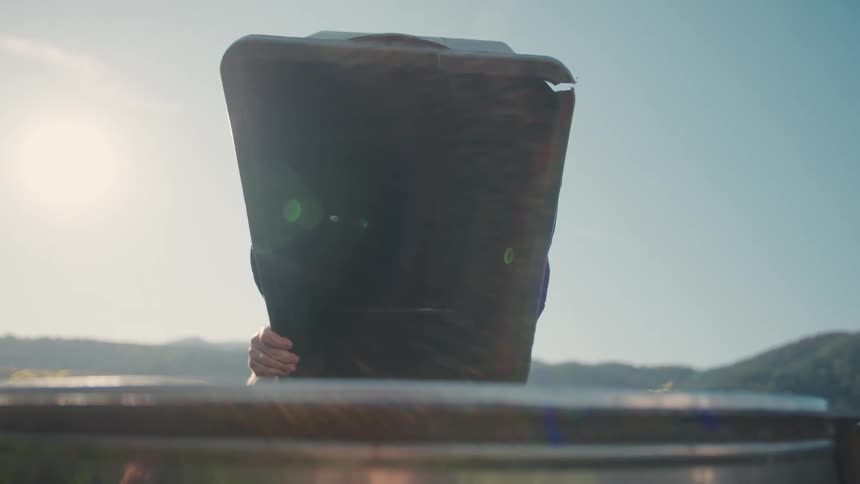 A person empties a harvest bin full of grapes into a large barrel under the bright sun