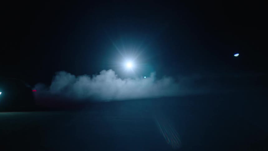 A car driving really fast at night in a lot and there is smoke coming out the back