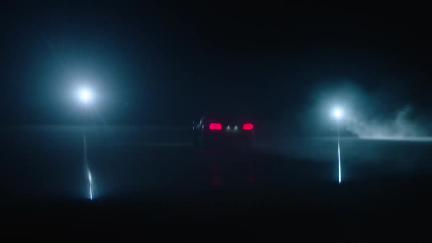 Car driving fast at night while bright lights shine in the distance
