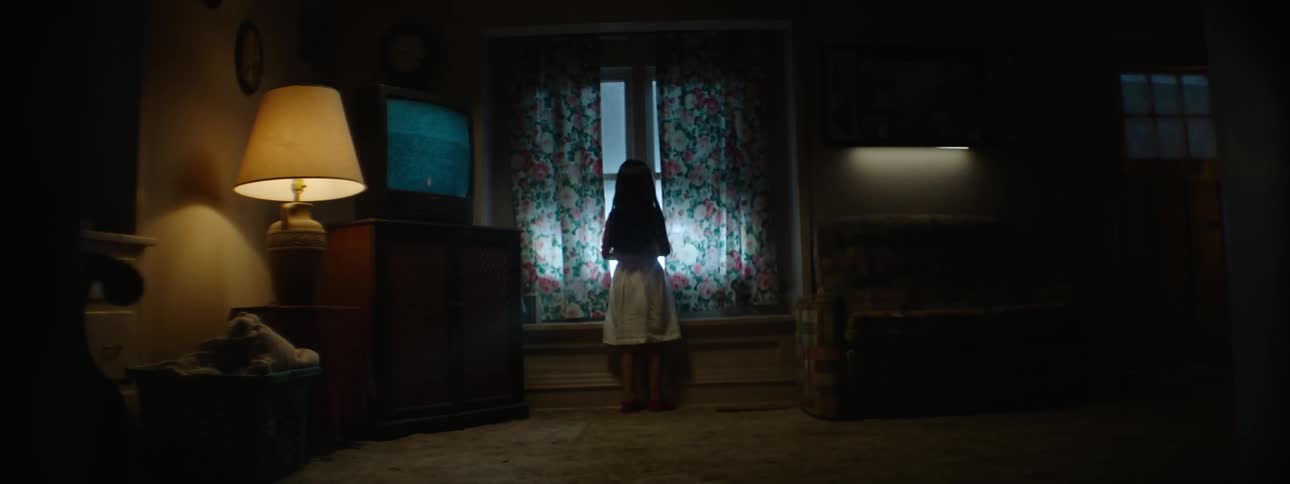Child in a dark living room at night looks at lights flashing at the window
