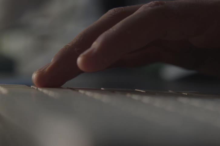 A closeup shows a hand gently pressing keys on a keyboard in soft light