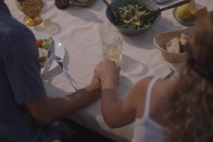 A young couple holding hands while sitting together at a dining table