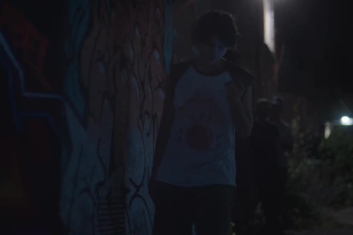Young man leaning against a graffiti wall talks on the phone at night