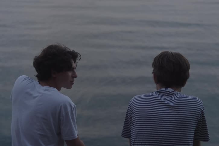 Two young men talk by the seaside at dusk
