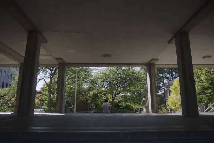 Man sitting under a concrete structure looking at sunlit trees
