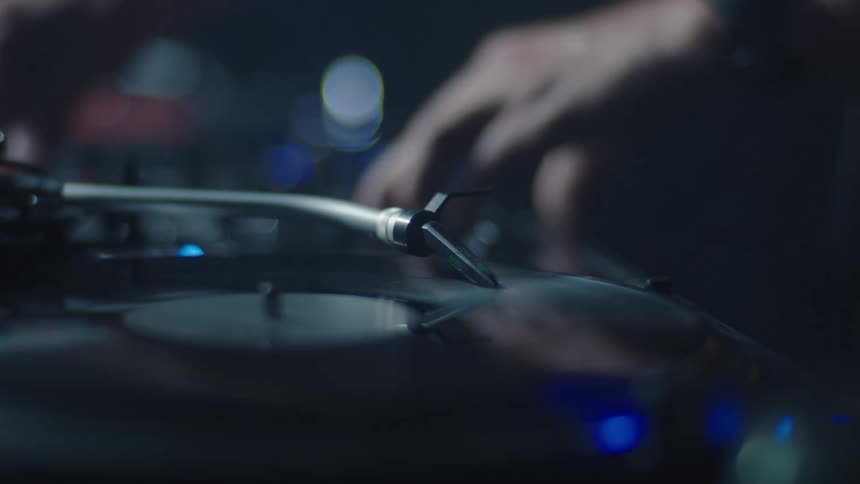 Close up of a dj operating a turntable in a club at night