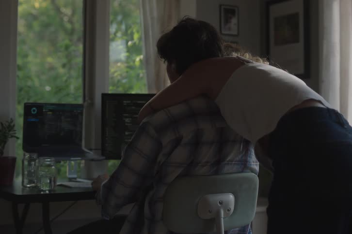 The woman hugs a man sitting at the desk