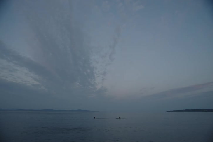 Two people swimming together in a large body of water outdoors at dusk