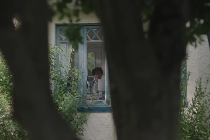 The man is sitting by the window at a desk inside