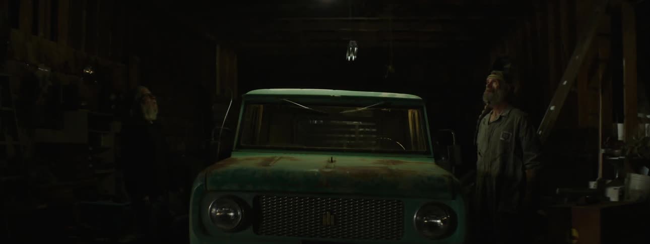 Two men stand beside a truck as the garage lights flicker