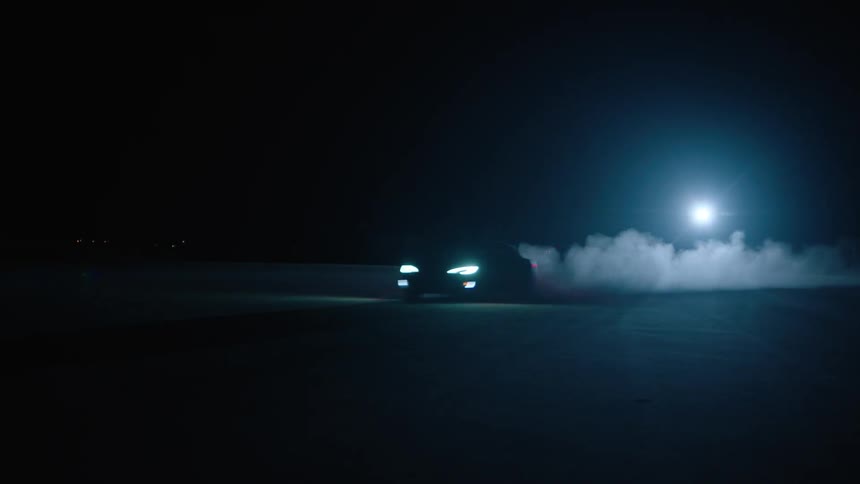 A car drives with its headlights on at night