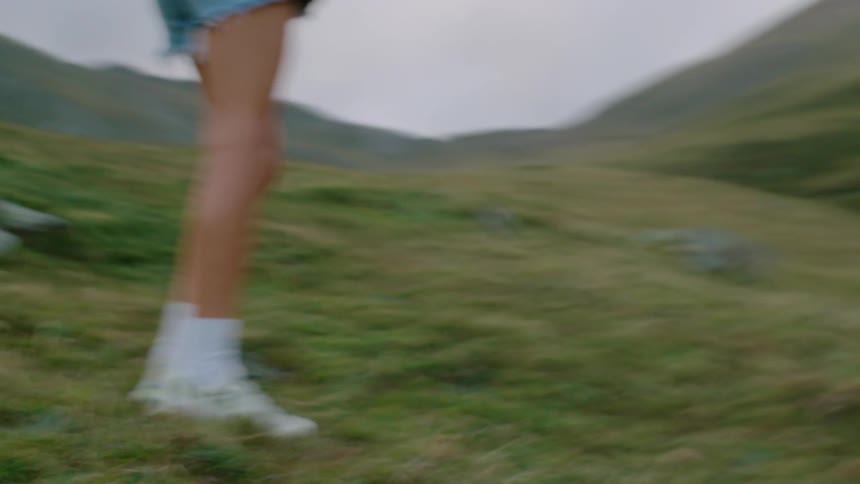 A pair of legs in white socks and sneakers blur in motion across a grassy hillside
