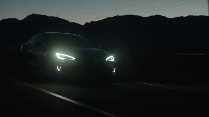 A car driving down a road at dusk with its headlights on