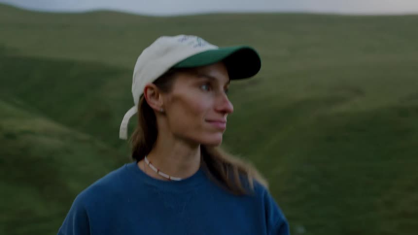 Person wearing a cap and blue sweatshirt among green hills