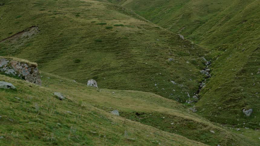 Grasscovered valley with rocks and a small stream between the hills