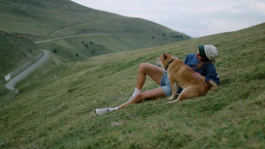 Woman sitting on a hillside with a child and a dog surrounded by green hills