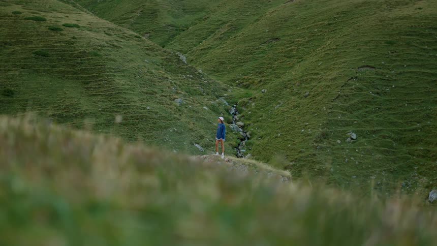 Person standing on a trail surrounded by green hills