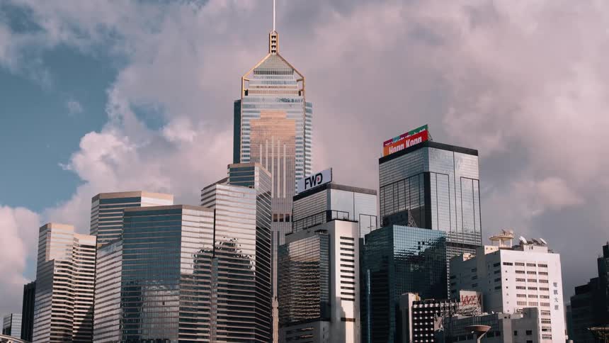 A city skyline features a series of skyscrapers at midday with digital billboards displaying ads on the rooftops of two buildings